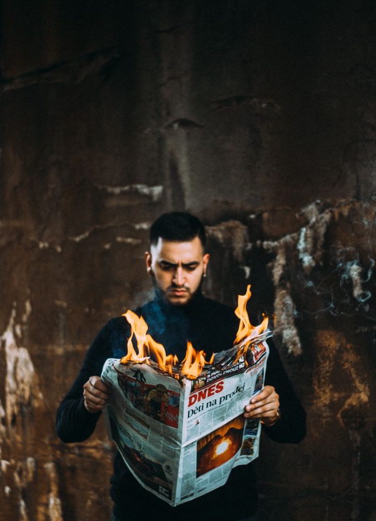 A man looks at a burning newspaper - representing the destruction of democracy, the tools of autocracy, the burning of truth